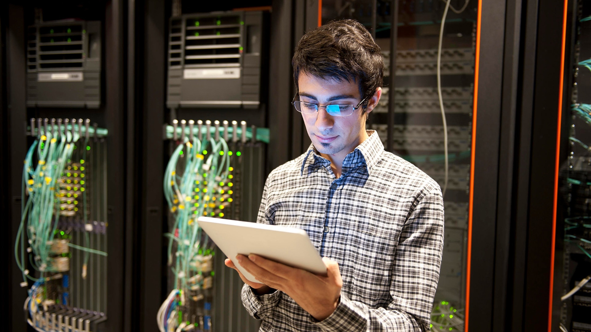 Technician looking at tablet device in front of server cabinet