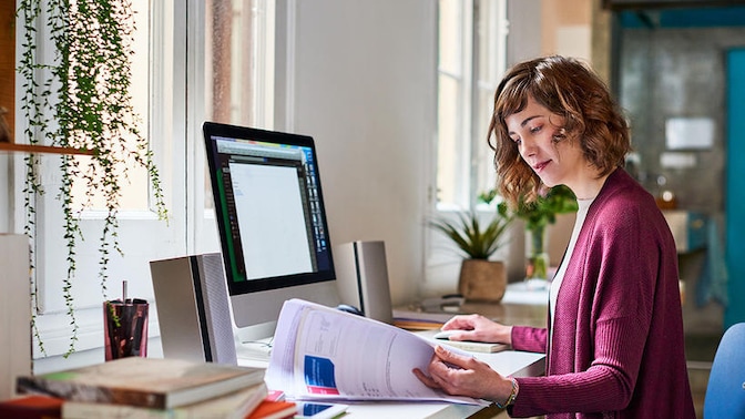 Woman sat at desk in front of computer browsing through print-outs