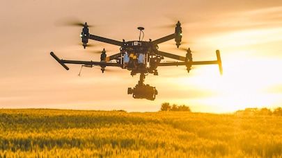 A drone flying over a field with a sunset in the background.