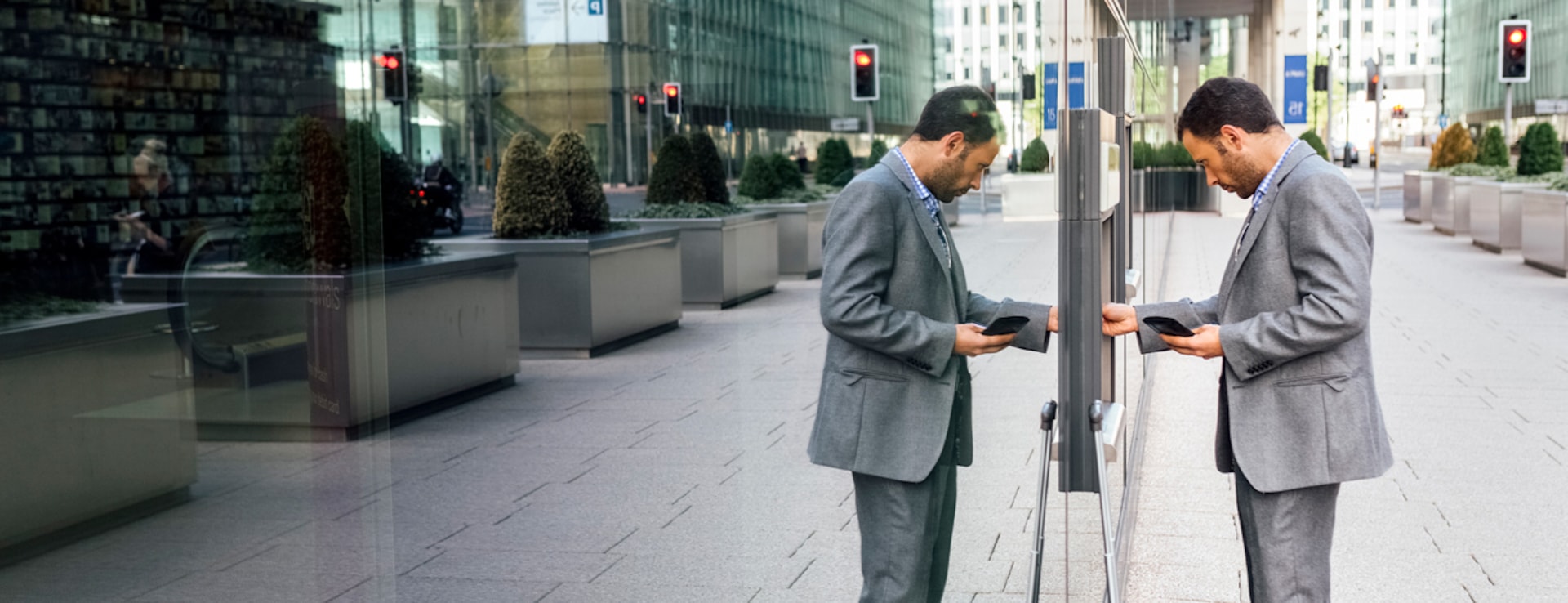 A person standing at an ATM with their reflection showing on a glass wall next to the ATM.