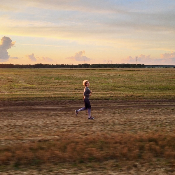 Woman jogging through field with electricity pl;ons on the horizon