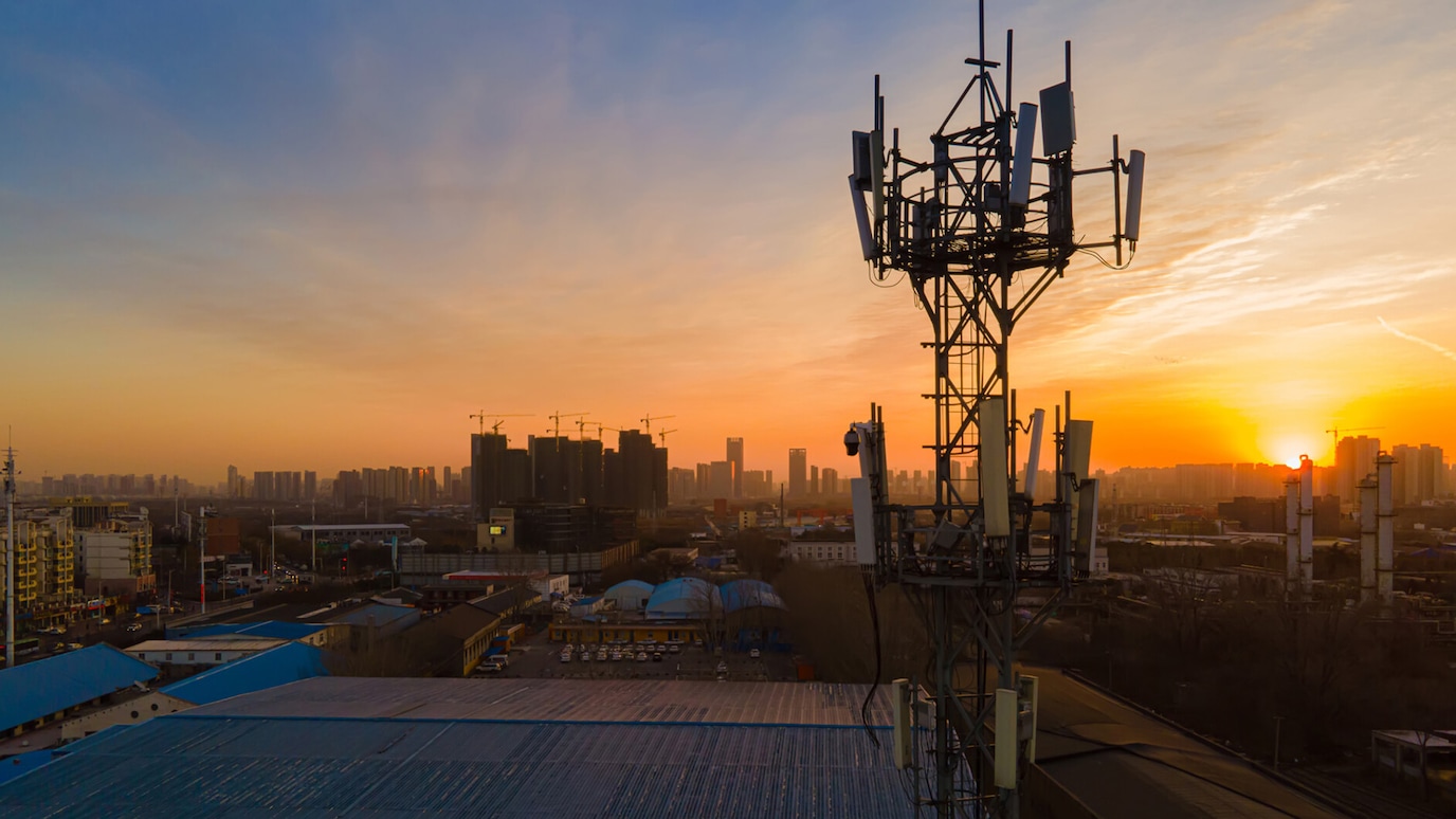 Antenna tower silhouetted against sunset with city skyline in background