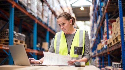 Warehouse operative in hi-viz vest checks data on a laptop