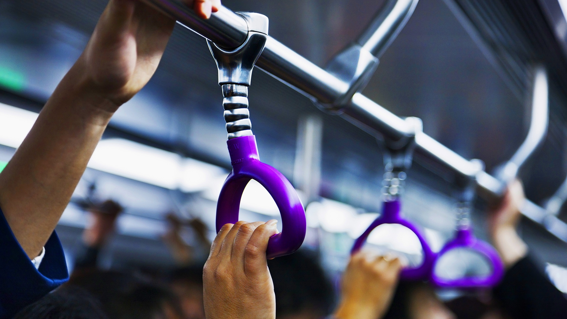 close up of people's hands holding onto an overhead handle on a train