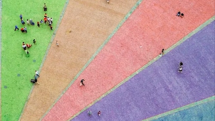 Arial shot of rainbow colours on the ground with people scattered across them