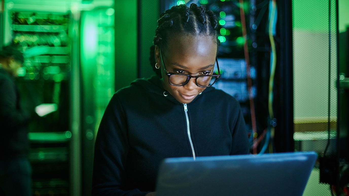 Programmer sitting in front of laptop in server room.