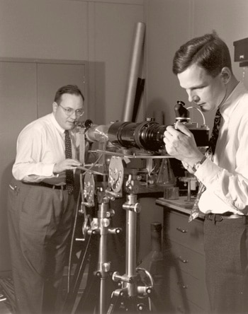 Arthur L Schawlow adjusts a ruby optical maser during an experiment at Bell Labs, while CGB Garrett prepares to photograph the maser flash