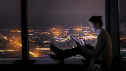 Woman sitting on widow seat in tall city building using tablet device