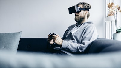 Man on sofa with console game controller wearing VR headset