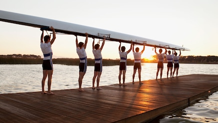 Eight people holding up a canoe on a dock