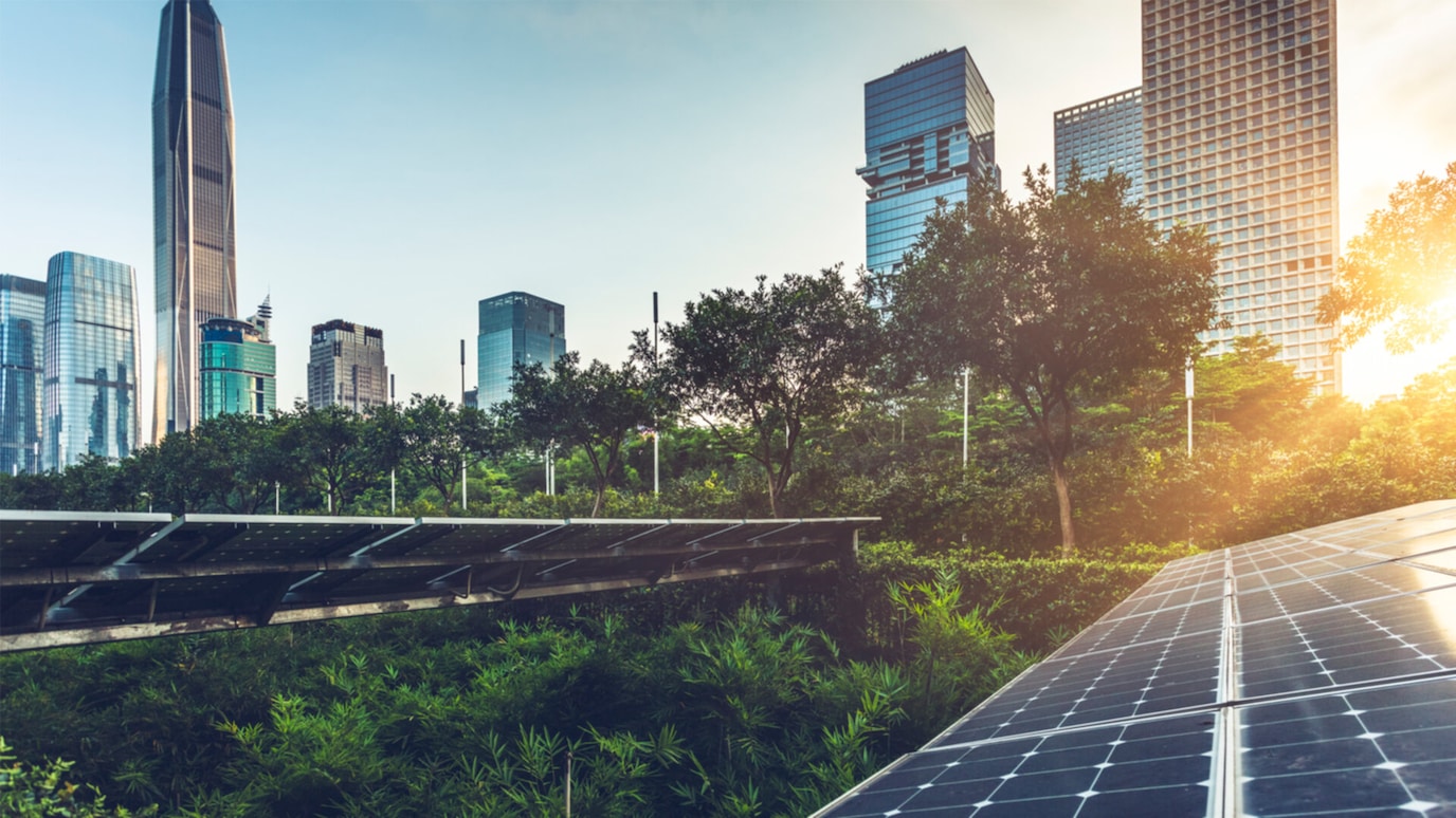 A cityscape with tall buildings and lush greenery. In the foreground, a solar panel array is capturing energy from the sun.