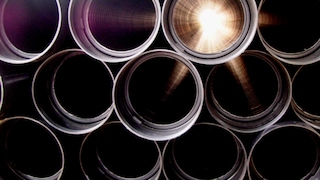 A close-up of a stack of black pipes, with one pipe in the center illuminated by a bright light.