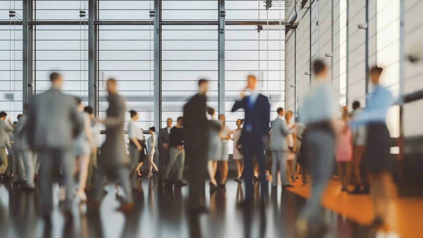 A large group of business professionals gathered in a modern, well-lit office space with floor-to-ceiling windows.