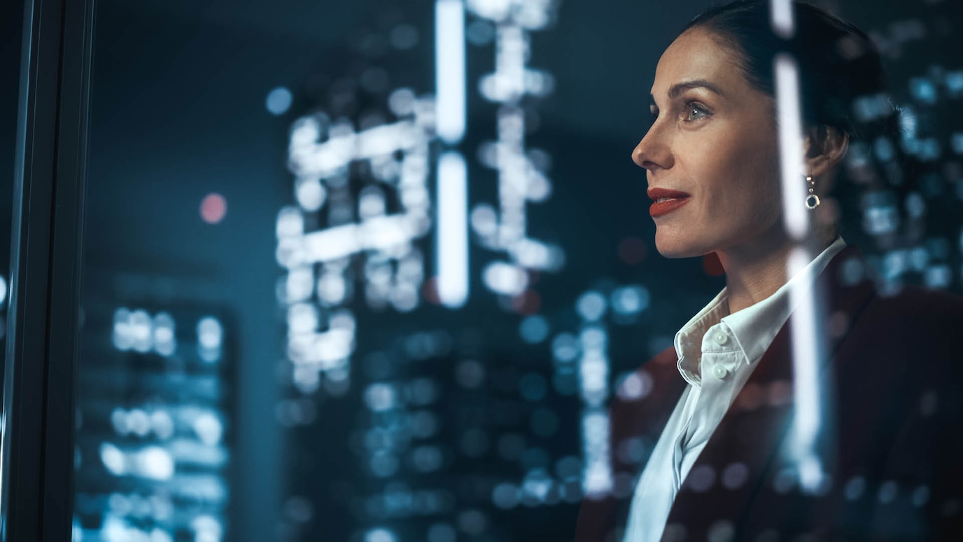 Woman looking out of window at skyscrapers at night