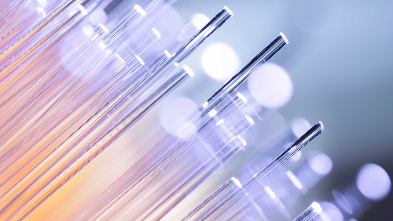 Close-up of glowing fiber optic cables with purple and orange hues against a blurred background with bokeh effect.