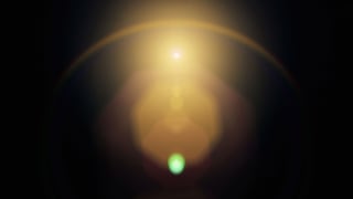 Abstract image of a bright golden light source with a halo effect against a dark background. A small green orb is visible at the bottom center, creating a contrast with the warm tones above.