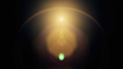 Abstract image of a bright golden light source with a halo effect against a dark background. A small green orb is visible at the bottom center, creating a contrast with the warm tones above.