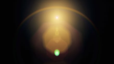 Abstract image of a bright golden light source with a halo effect against a dark background. A small green orb is visible at the bottom center, creating a contrast with the warm tones above.