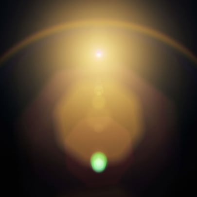 Abstract image of a bright golden light source with a halo effect against a dark background. A small green orb is visible at the bottom center, creating a contrast with the warm tones above.