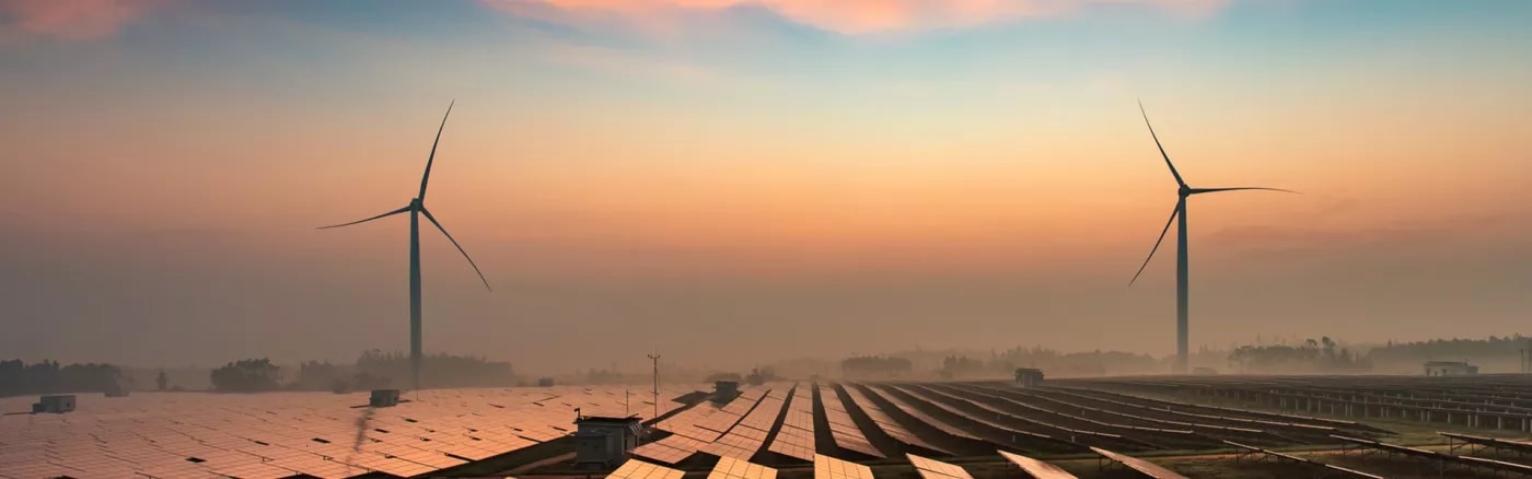 A picture of two wind turbines and many solar panels in a morning haze.