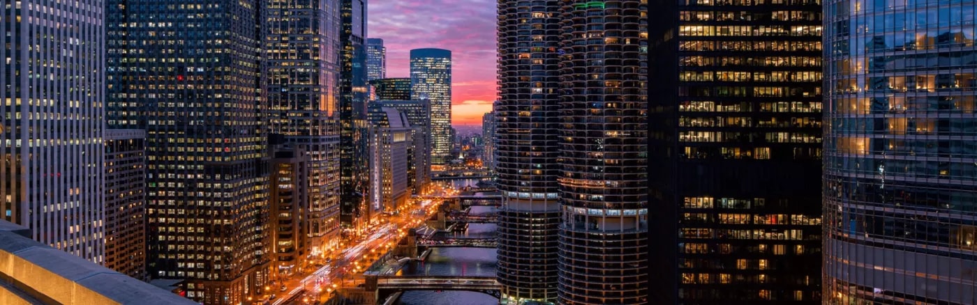 An image of a river with high-rise buildings on both sides of it and a sunset in the background.