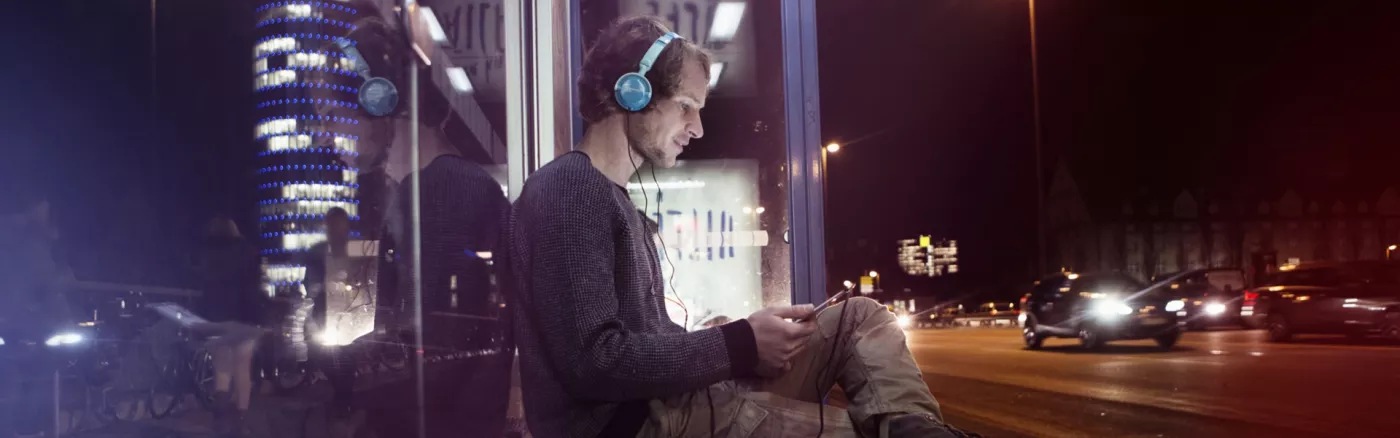 A person sitting at a bus stop at nighttime with their headphones on.