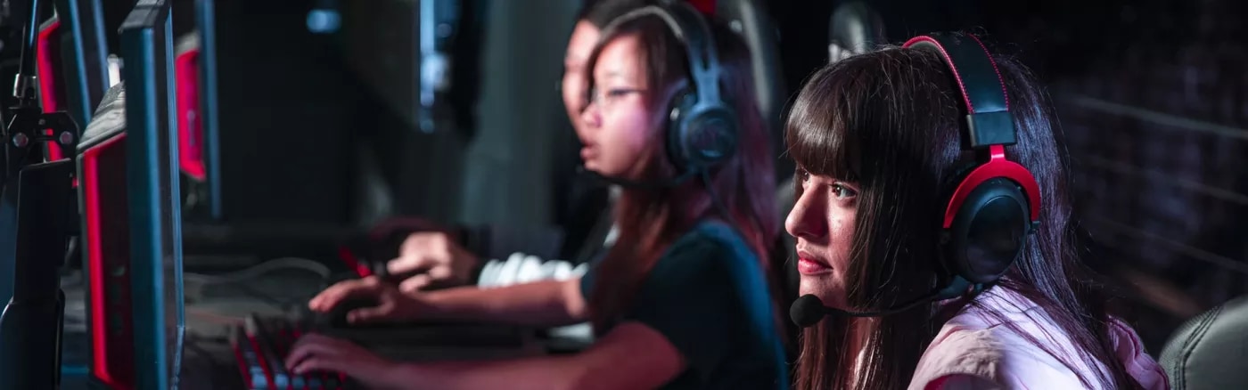 Three young people sitting by gaming PCs wearing headsets.