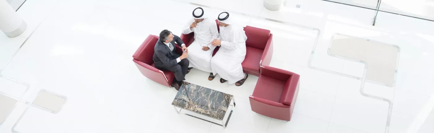 An image of three people sitting on red couches discussing something.