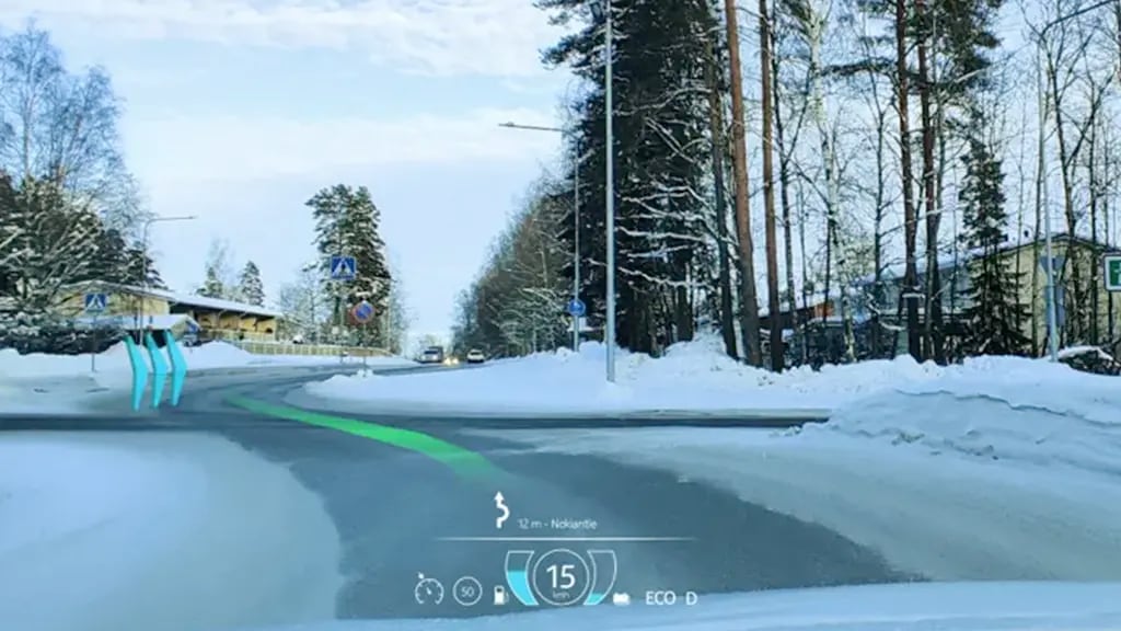 Car windshield view of snowy road with augmented reality overlay showing speed, driving mode, and navigation path. Blue markers highlight road ahead.