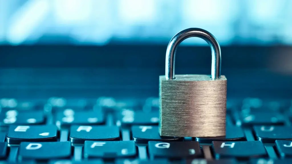 A silver padlock sits atop a black computer keyboard against a teal blue background. The image is shot in macro, showing fine detail of the lock's metallic texture while the keyboard keys blur into the background.