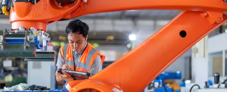 Male factory worker with tablet next to a robotic arm