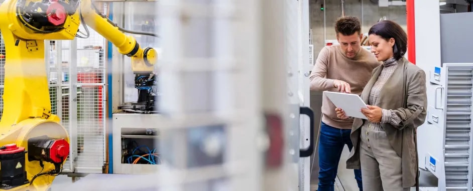 Colleagues working together in a plant, with a robotic arm device operating in the background