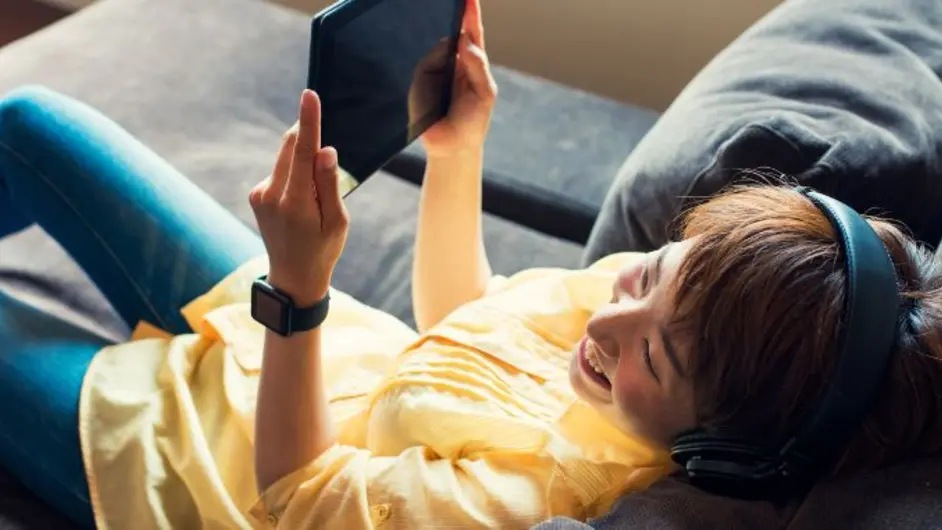 A woman enjoying music while gazing at a tablet.