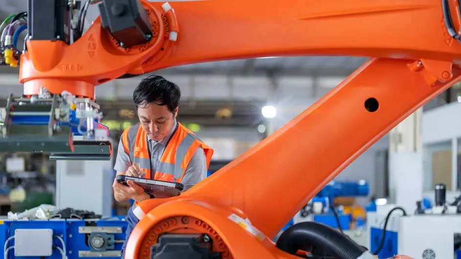 Male factory worker with tablet next to a robotic arm