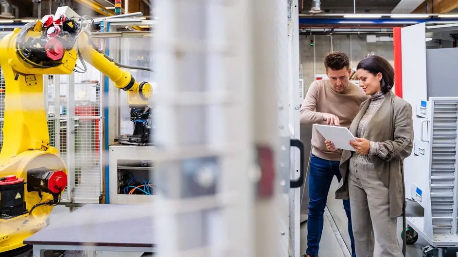 Colleagues working together in a plant, with a robotic arm device operating in the background