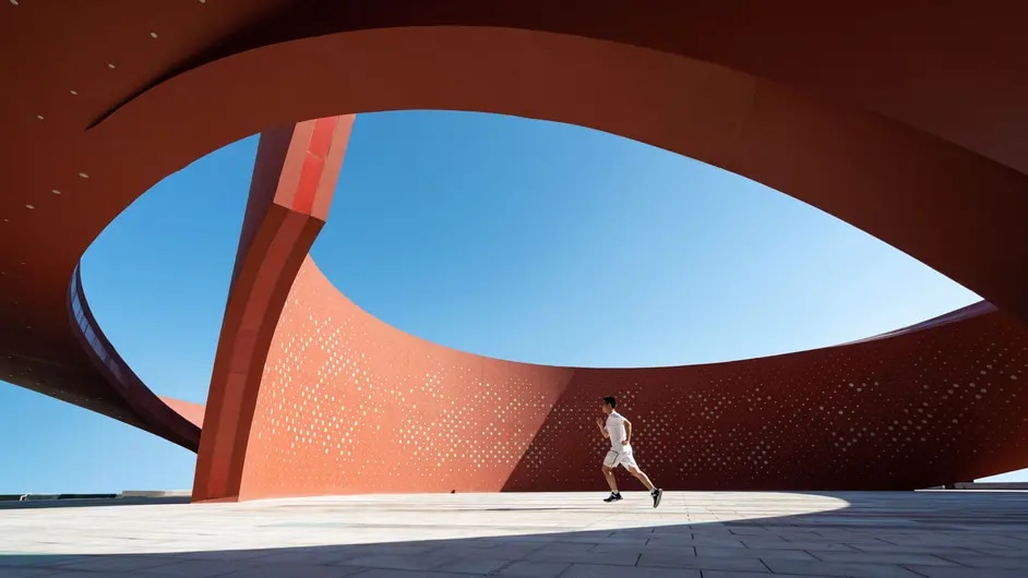 A striking piece of modern architecture featuring a large, curved orange structure with an eye-shaped opening that frames a bright blue sky.