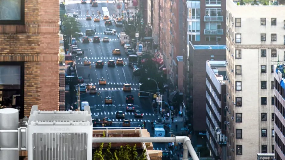 An urban scene from a high vantage point, overlooking a busy city street lined with buildings. In the foreground, there is a Nokia radio antenna installation on a rooftop, highlighting the integration of modern telecommunications infrastructure within the cityscape