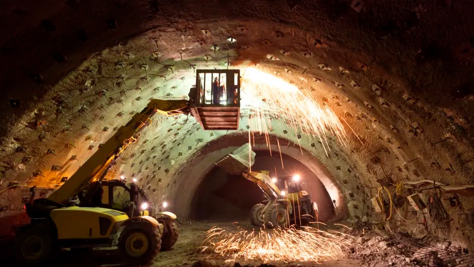 An underground construction: Arched tunnel with workers on suspended platform welding, sparks flying.
