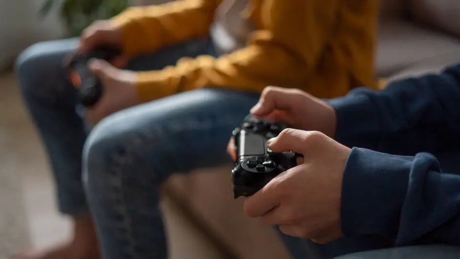 Close-up shot of hands holding video game controllers. Two people sit side by side in casual clothing playing video games together.